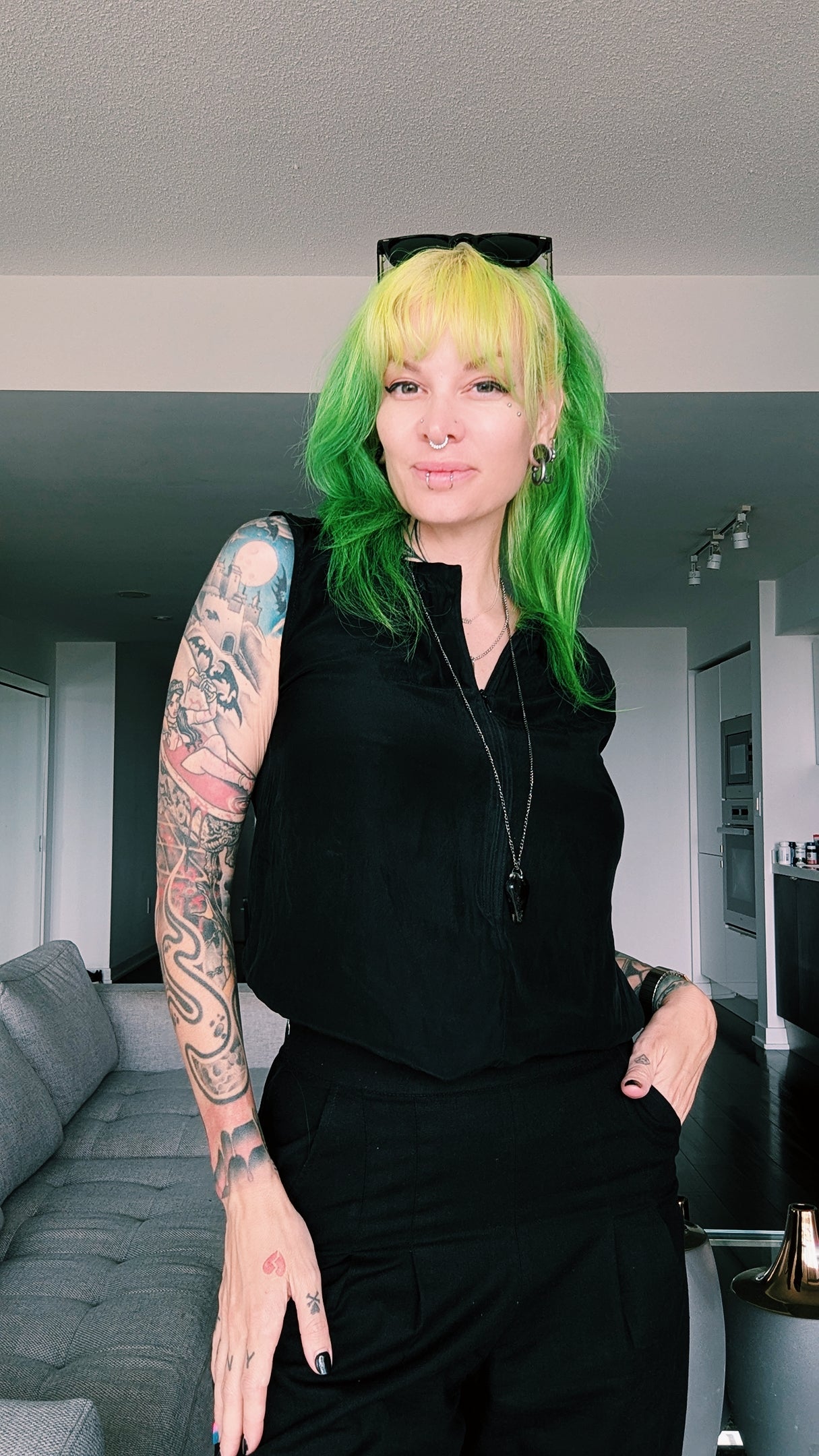 Photo of Verona, the owner, she his wearing a black outfit, and has shoulder length green hair and tattoos on her arms