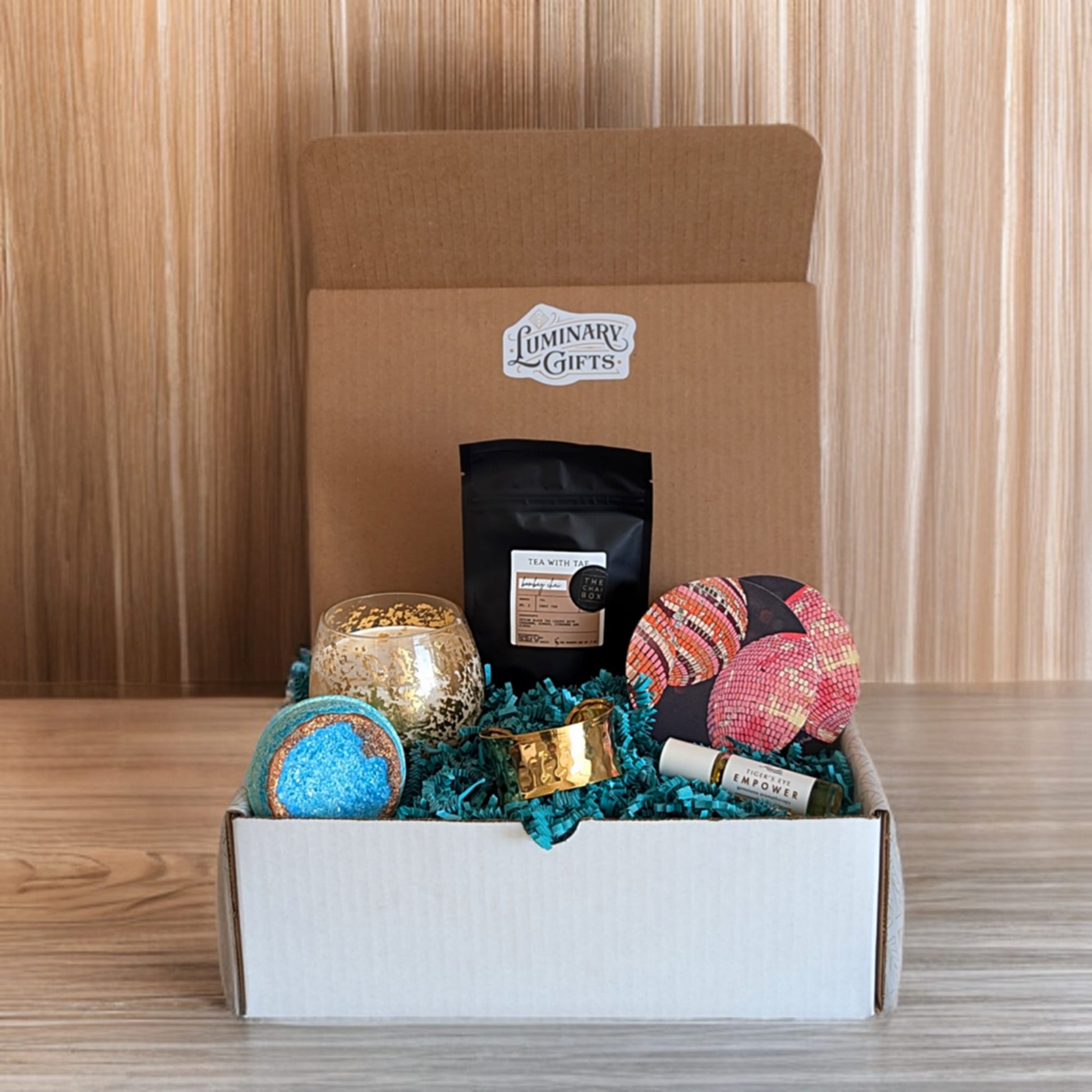 Celebration box contains chai tea, disco coasters, empower tigers eye oil roller, brass bangle, gold leaf candle and a blue geode bath bomb