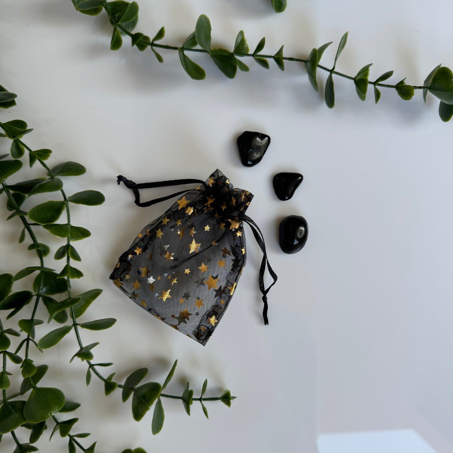 A black mesh bag with gold stars lays on a white background next to 3 "apache tears" rocks - they are roundish, about an inch across, and shiny black