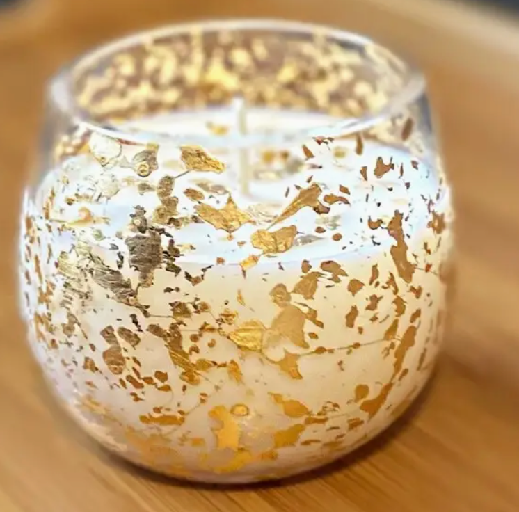 White candle in a glass vessel flecked wiht gold leaf